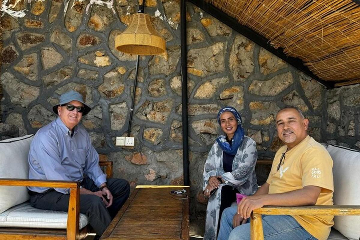 três pessoas sentadas em frente a um muro de pedra