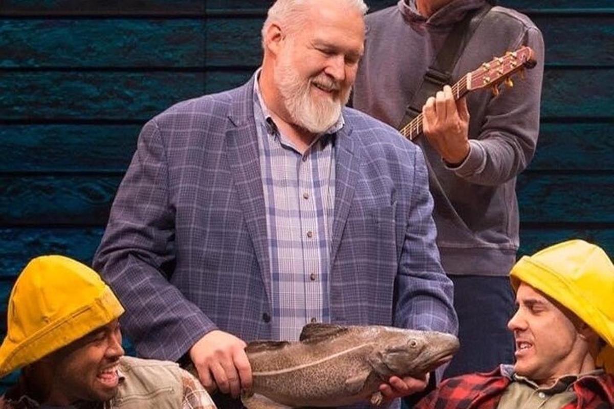 a man holding a fish in front of a group of people