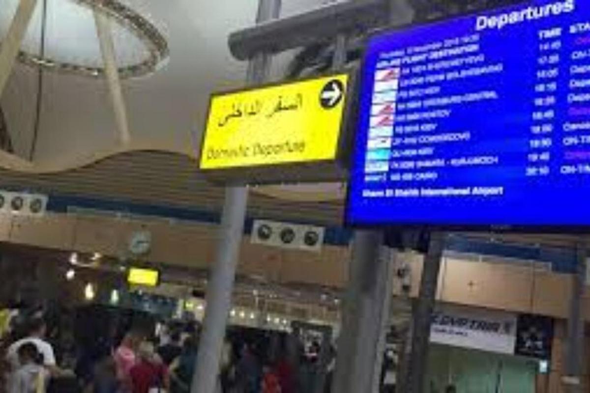 a sign in an airport with people walking around