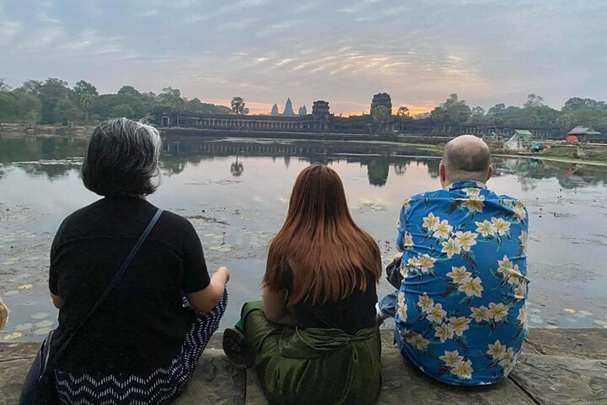 tres personas sentadas en el borde de un cuerpo de agua