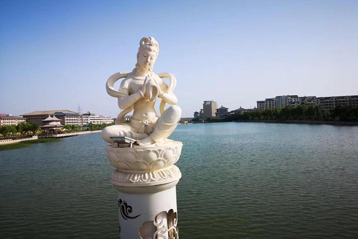 a statue of a woman sitting on a pole next to water