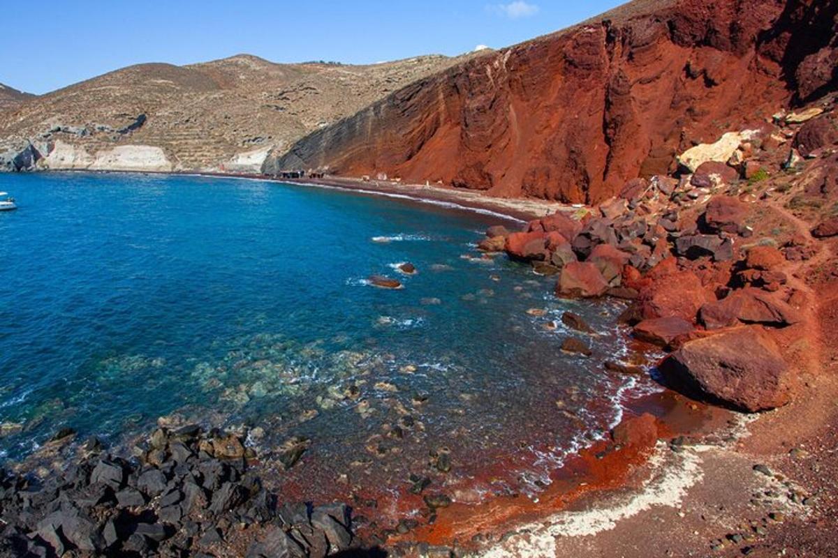 een strand met rotsen en blauw water en een berg