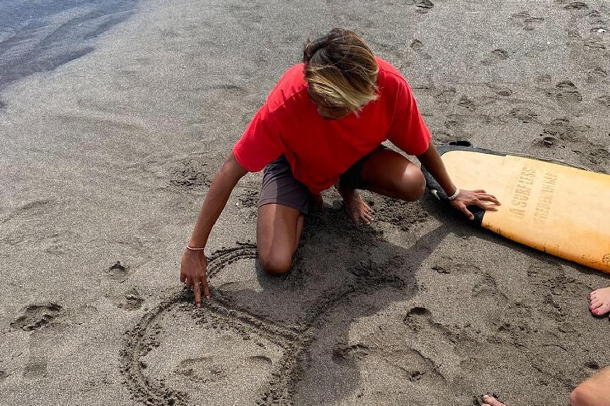 a woman drawing in the sand on the beach with a surfboard