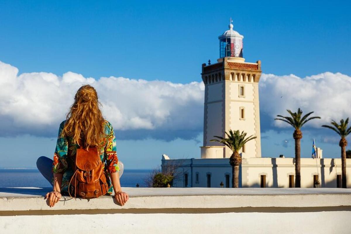 una donna seduta su un muro di fronte a un faro