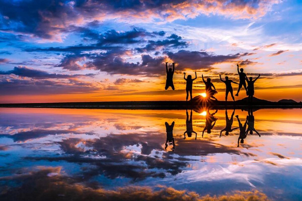 a group of people jumping in the water at sunset