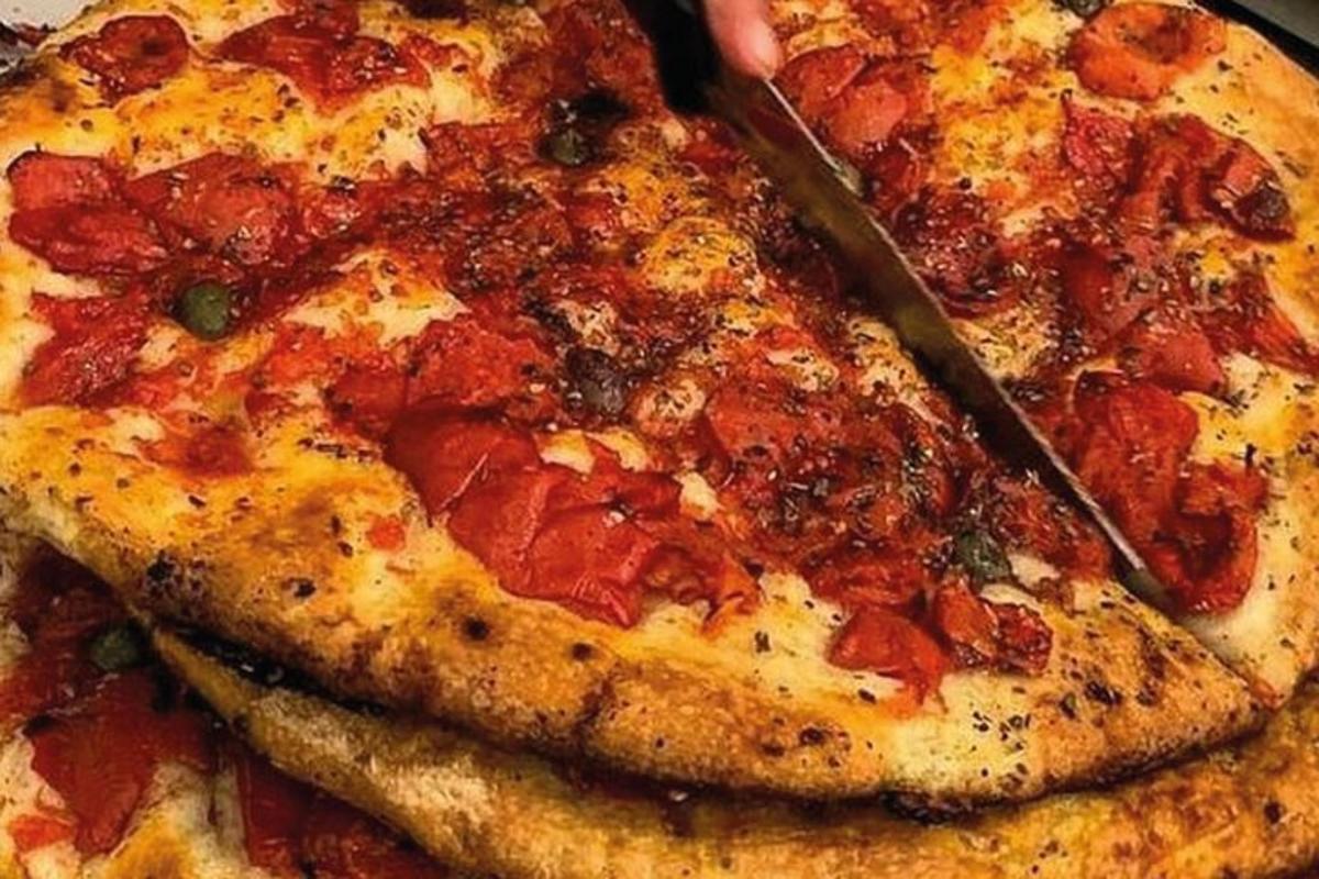 a person cutting a pizza with a knife