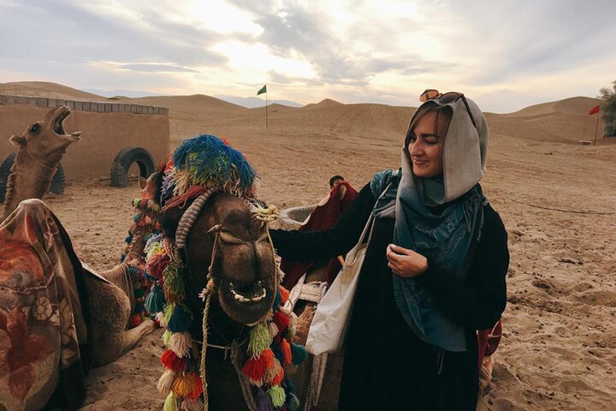 Una mujer parada junto a un camello en el desierto.