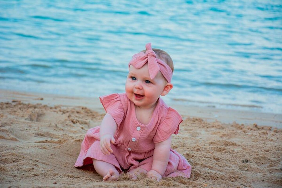 một bé gái đang ngồi trên cát trên bãi biển