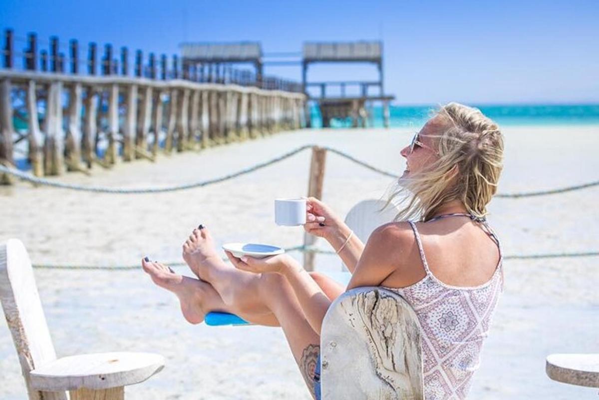uma mulher sentada na praia com uma xícara de café