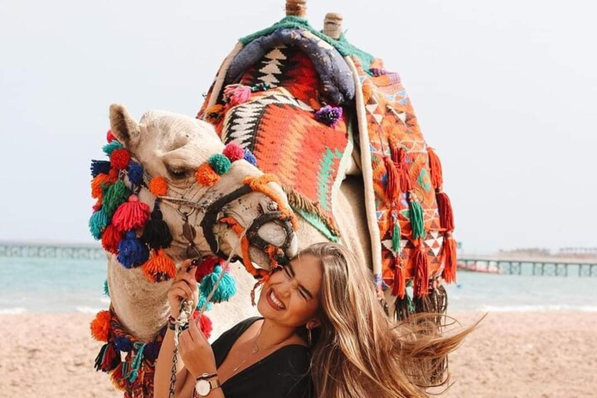 Una mujer parada junto a un camello decorado en la playa.