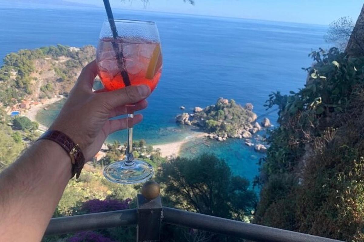 en person som holder et glass vin foran havet