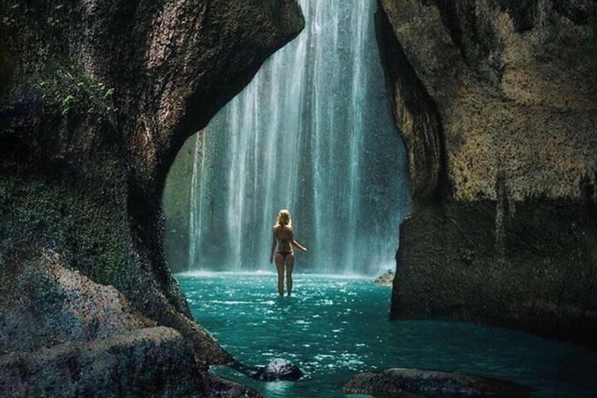 a woman walking through water in front of a waterfall