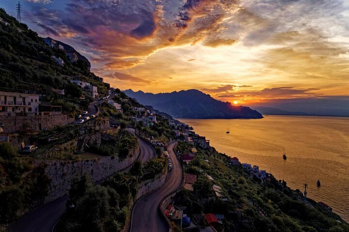 un tramonto su una collina con una strada accanto all'acqua
