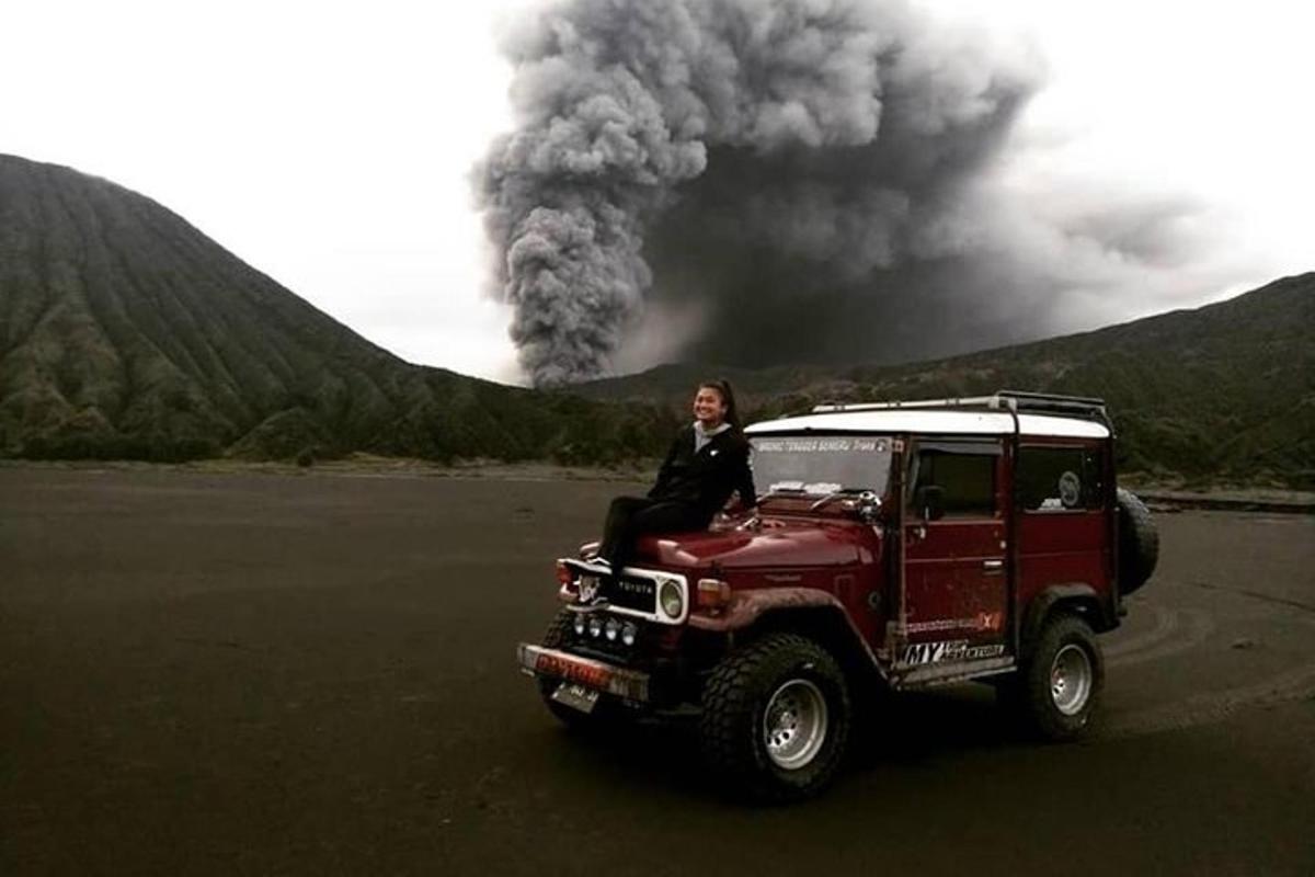 a woman sitting in a red jeep with smoke in the background