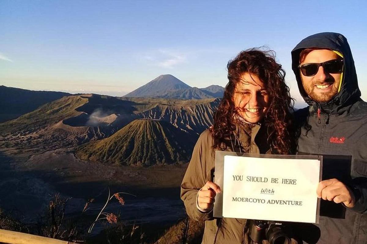 a man and woman holding up a sign on top of a mountain