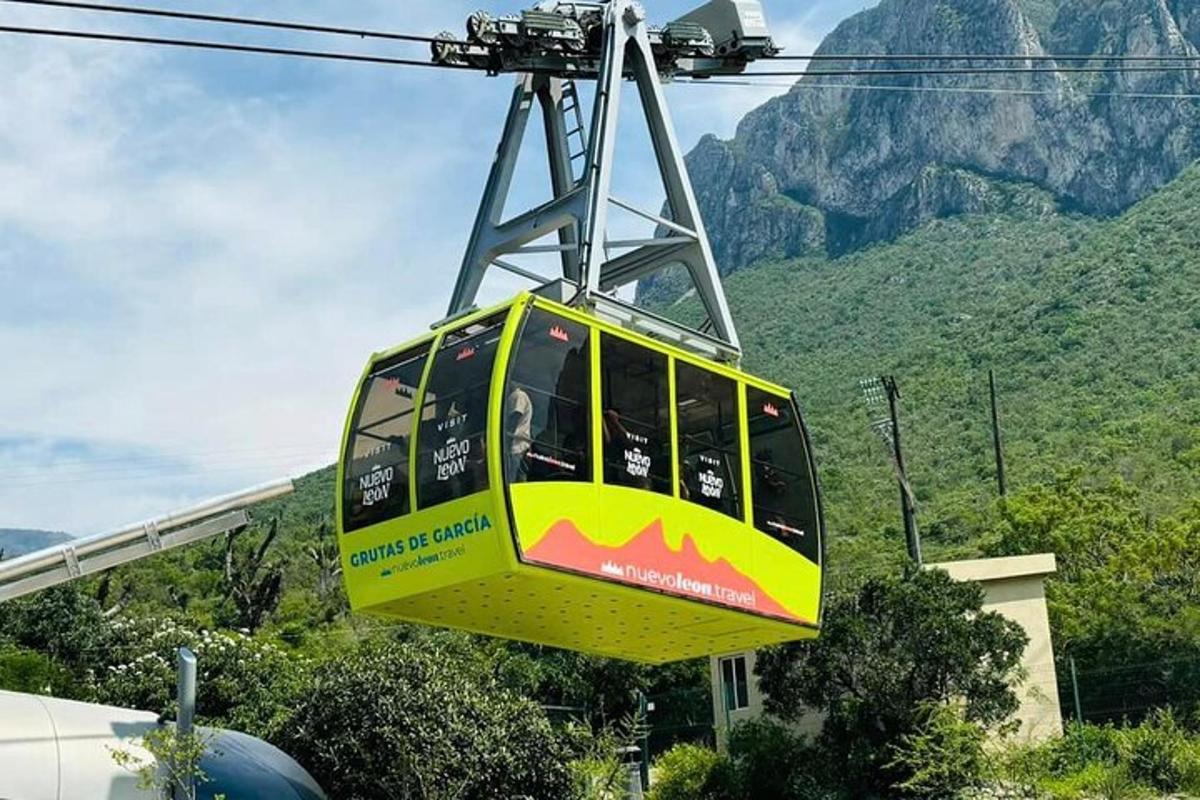 a yellow and green cable car in front of a mountain