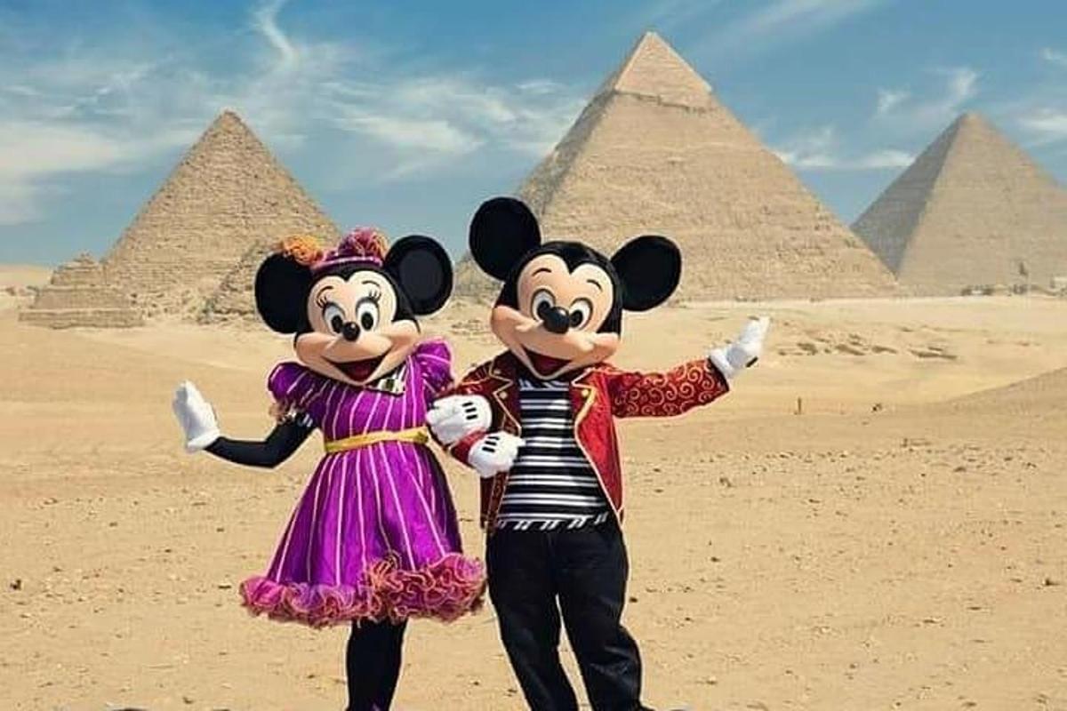Două persoane în costume de Mickey Mouse stând în fața piramidelor