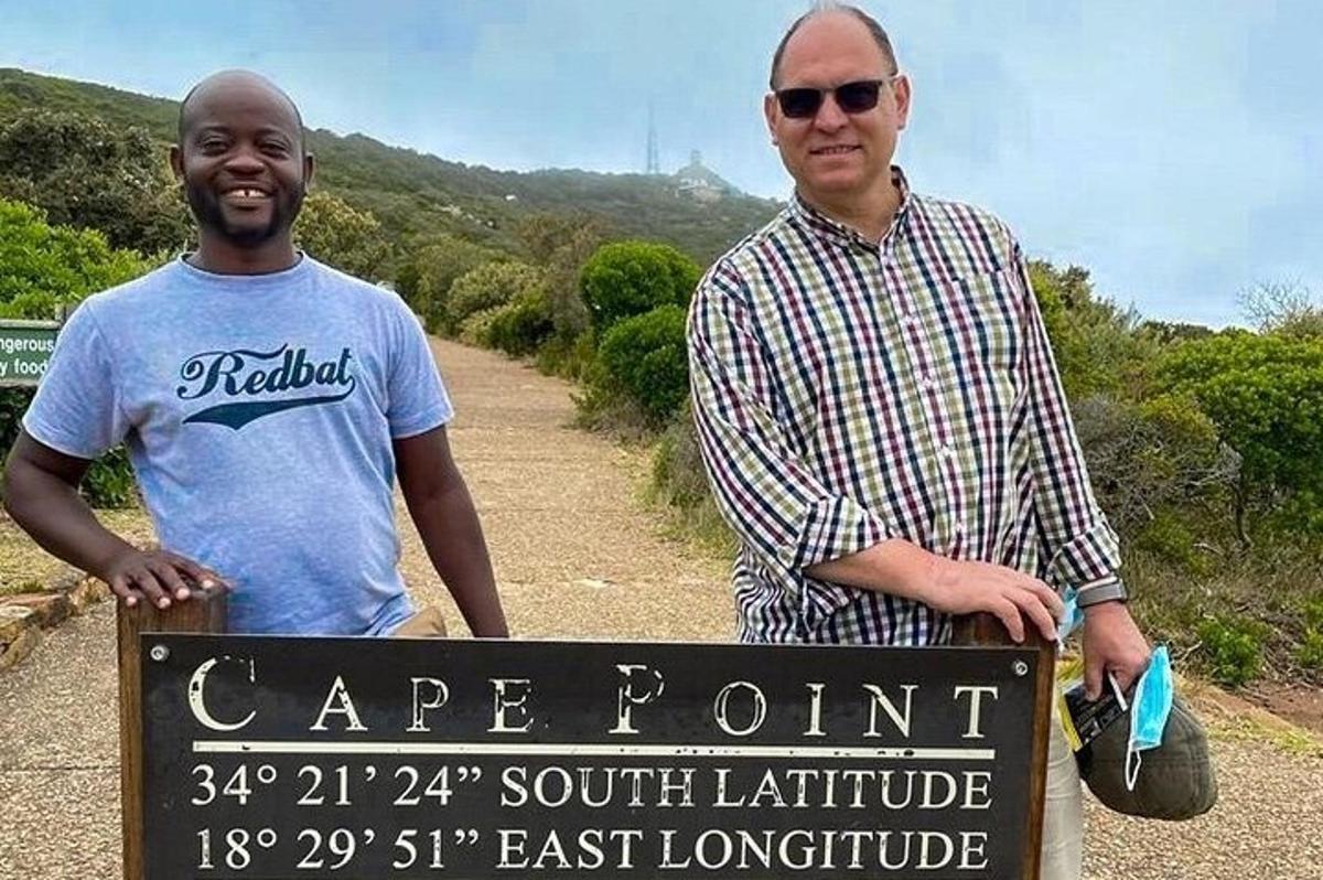 dois homens parados ao lado de uma placa ao lado de uma estrada