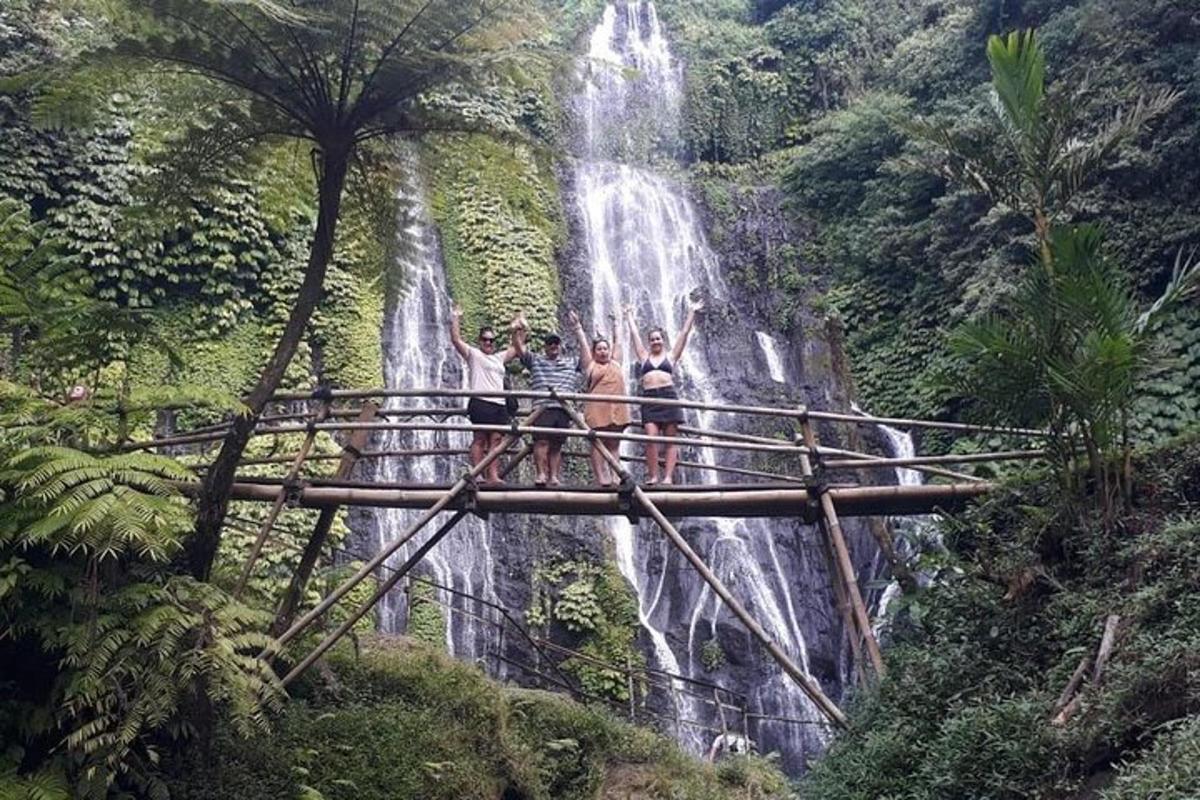 Tres personas de pie en un puente frente a una cascada.