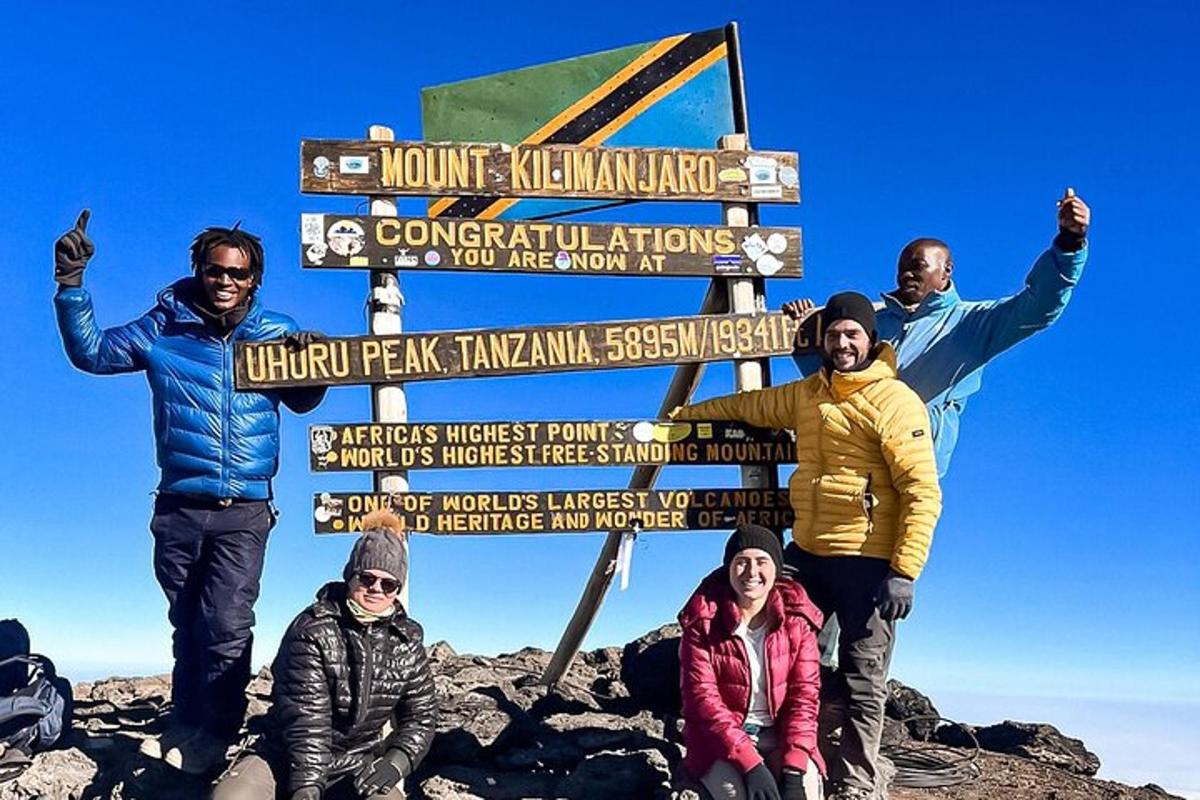 sekumpulan orang berdiri di sebelah papan tanda di atas gunung