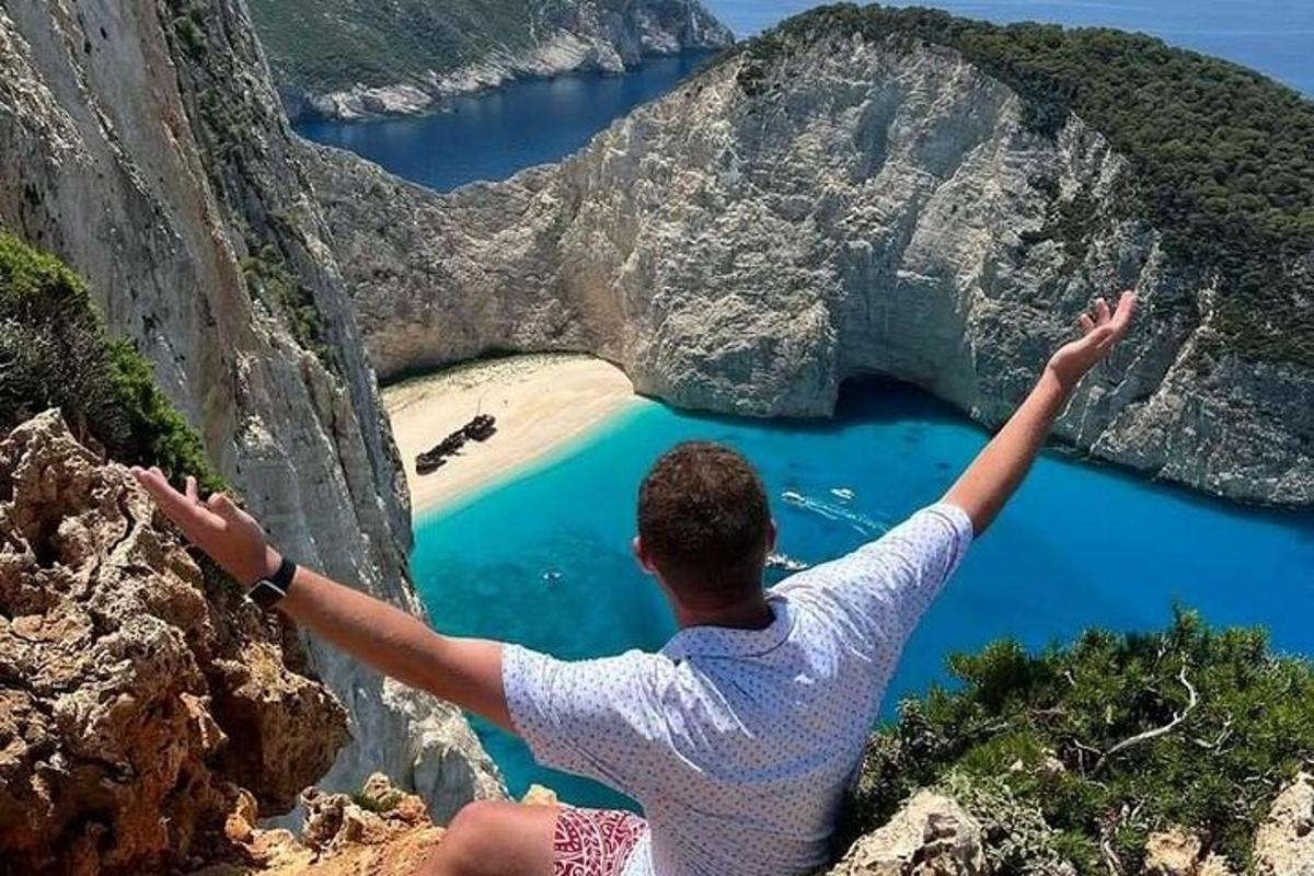 muž sedící na útesu s rozpaženýma rukama