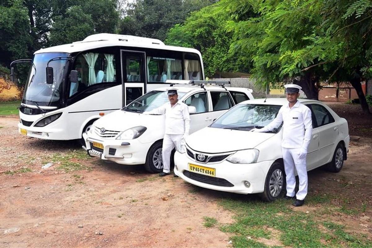 dos homes drets al costat de dos cotxes blancs i un autobús