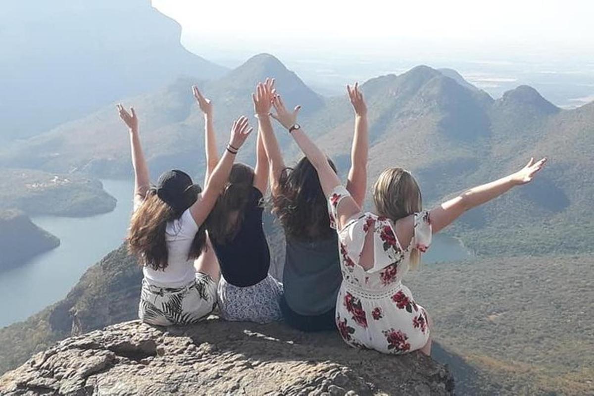 four girls sitting on a rock with their hands in the air