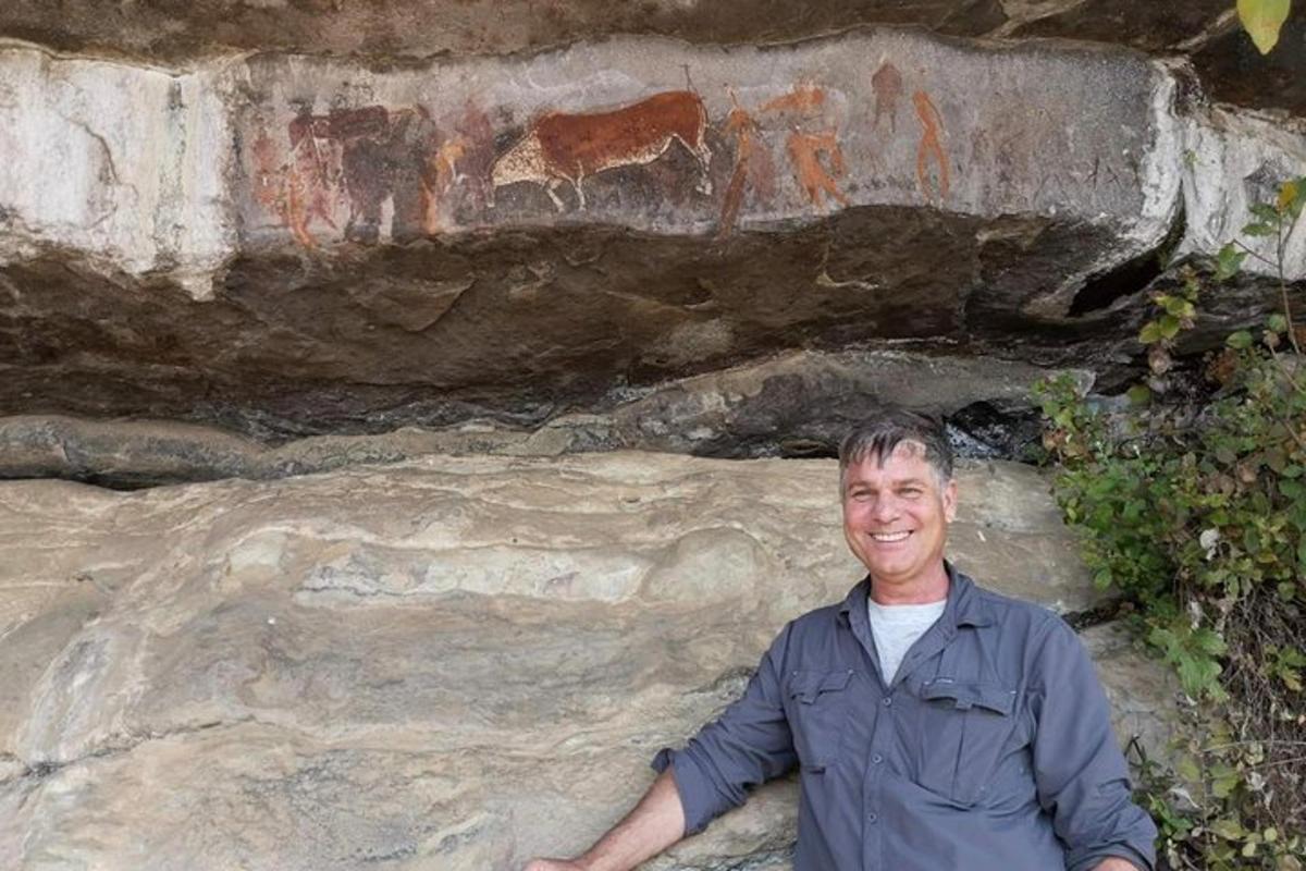 a man standing in front of a rock wall with paintings