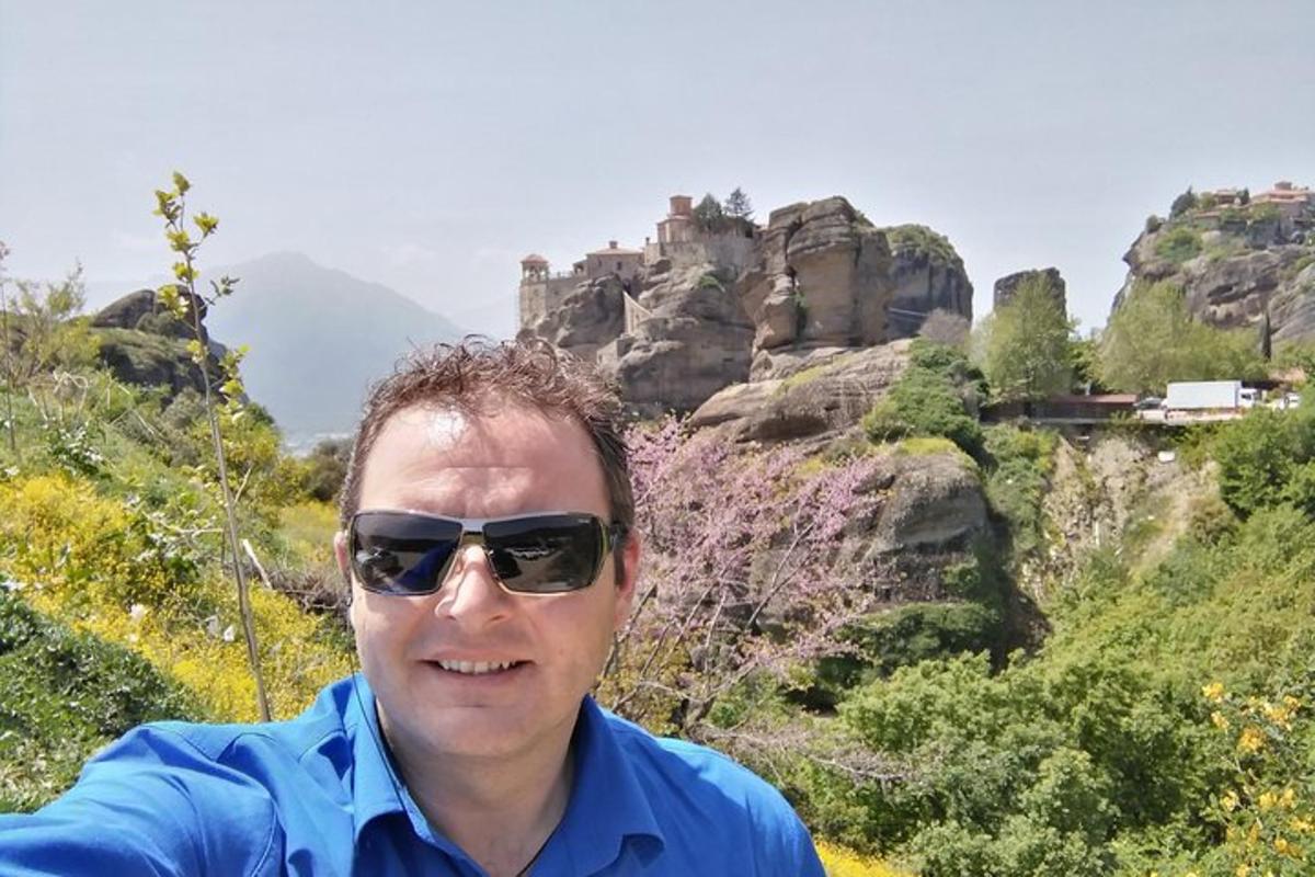 Ένας άντρας που φοράει γυαλιά ηλίου και στέκεται μπροστά σε ένα βουνό