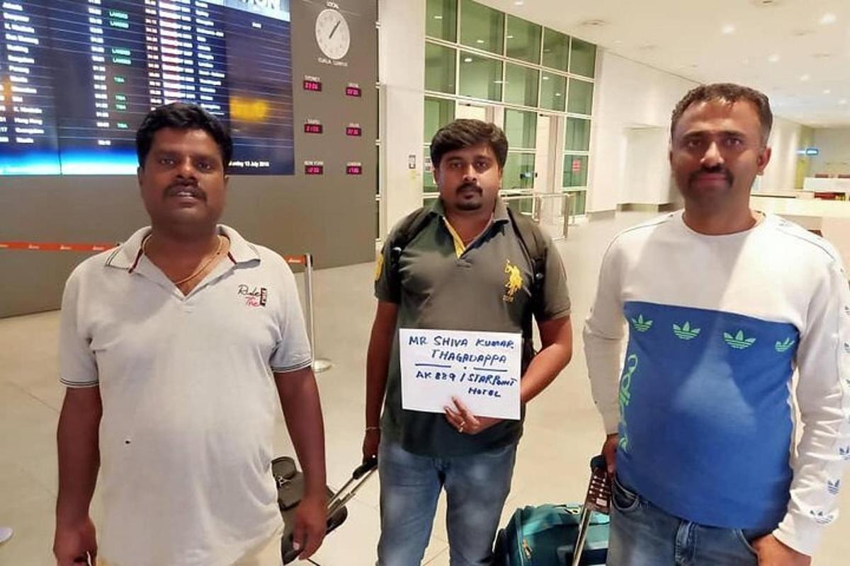 Tres hombres de pie en un aeropuerto sosteniendo un cartel