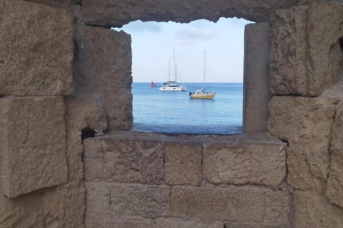 okno v kamenné zdi s výhledem na oceán s loděmi