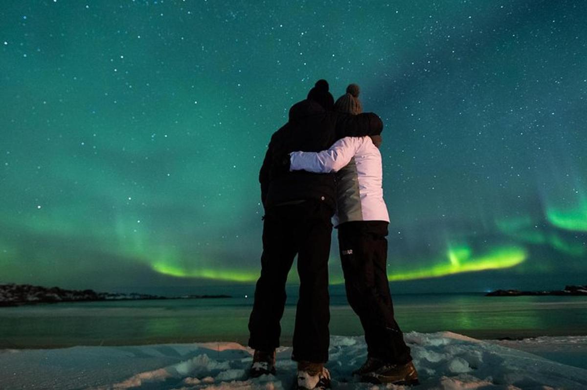 Maður og kona standa í snjónum undir norðurljósum