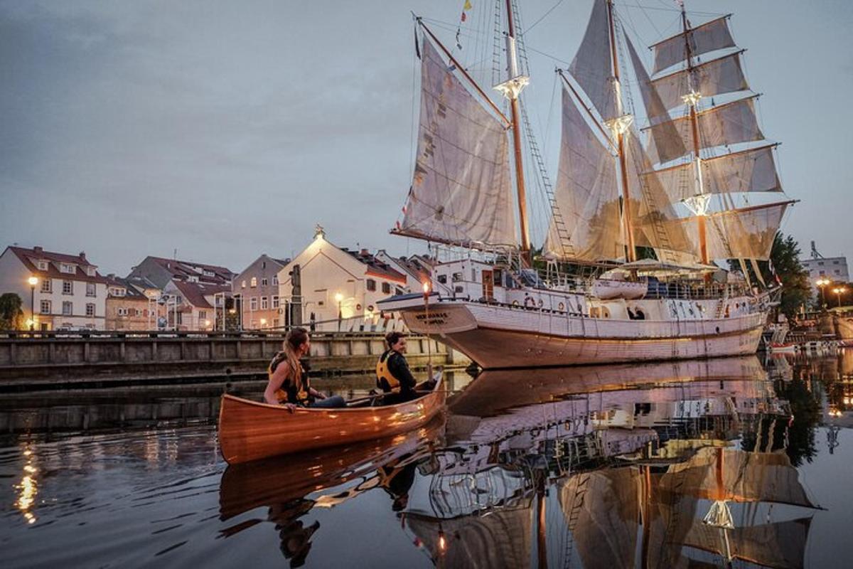 two people in a small boat next to a large sail boat