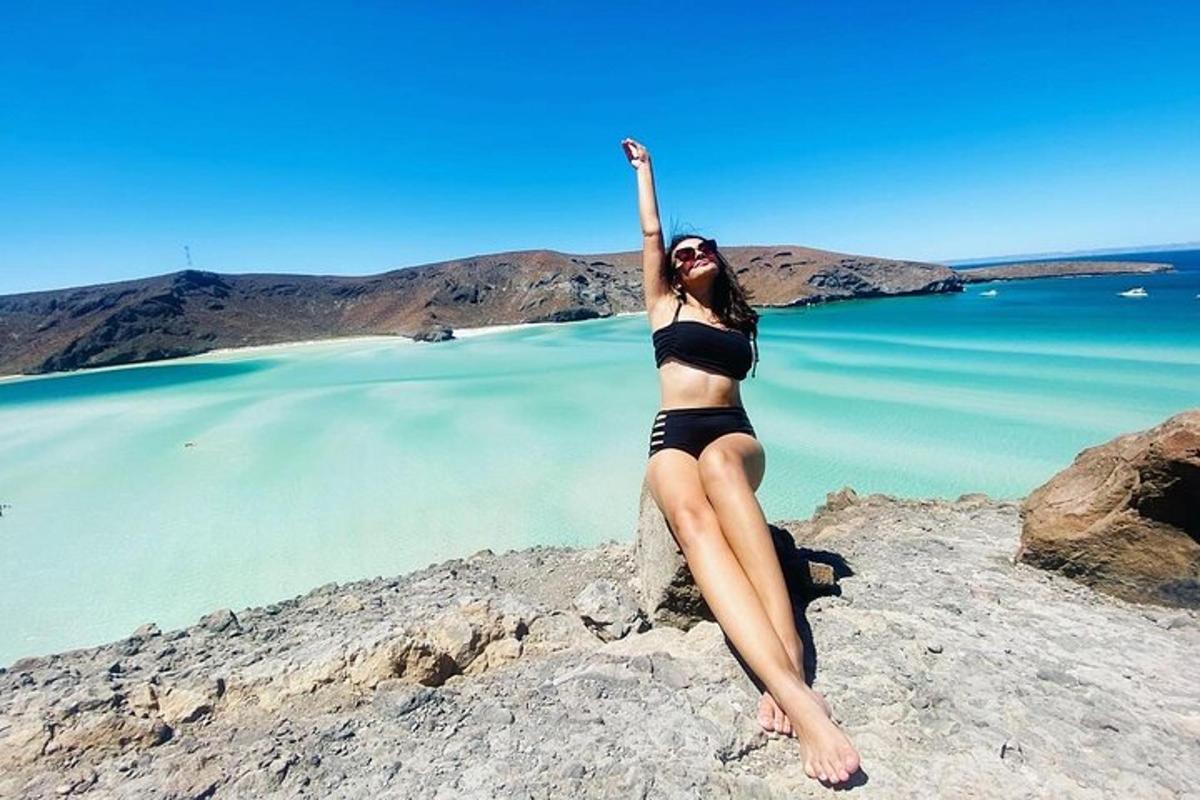 uma mulher de biquíni sentada em uma pedra perto da água