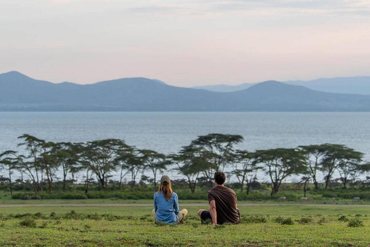 a man and woman sitting in a field looking at the ocean