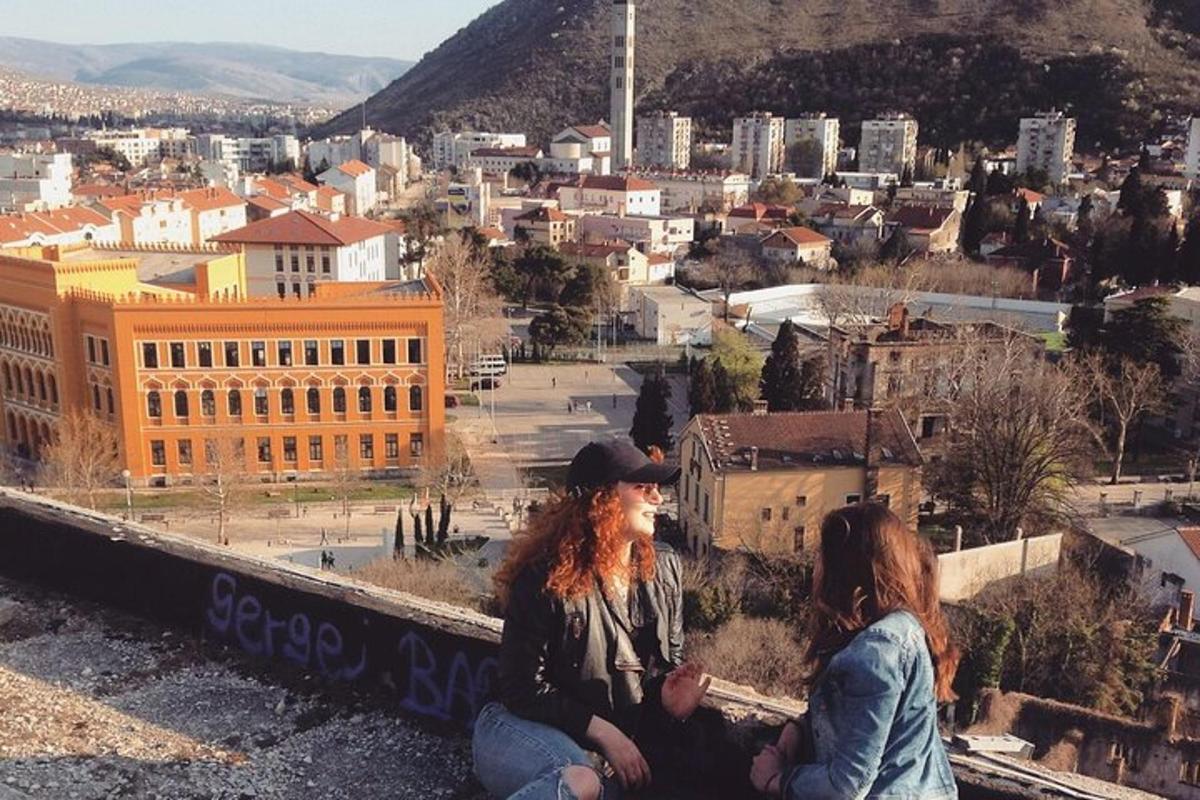 dve ženski, ki sedita na robu pobočja s pogledom na mesto