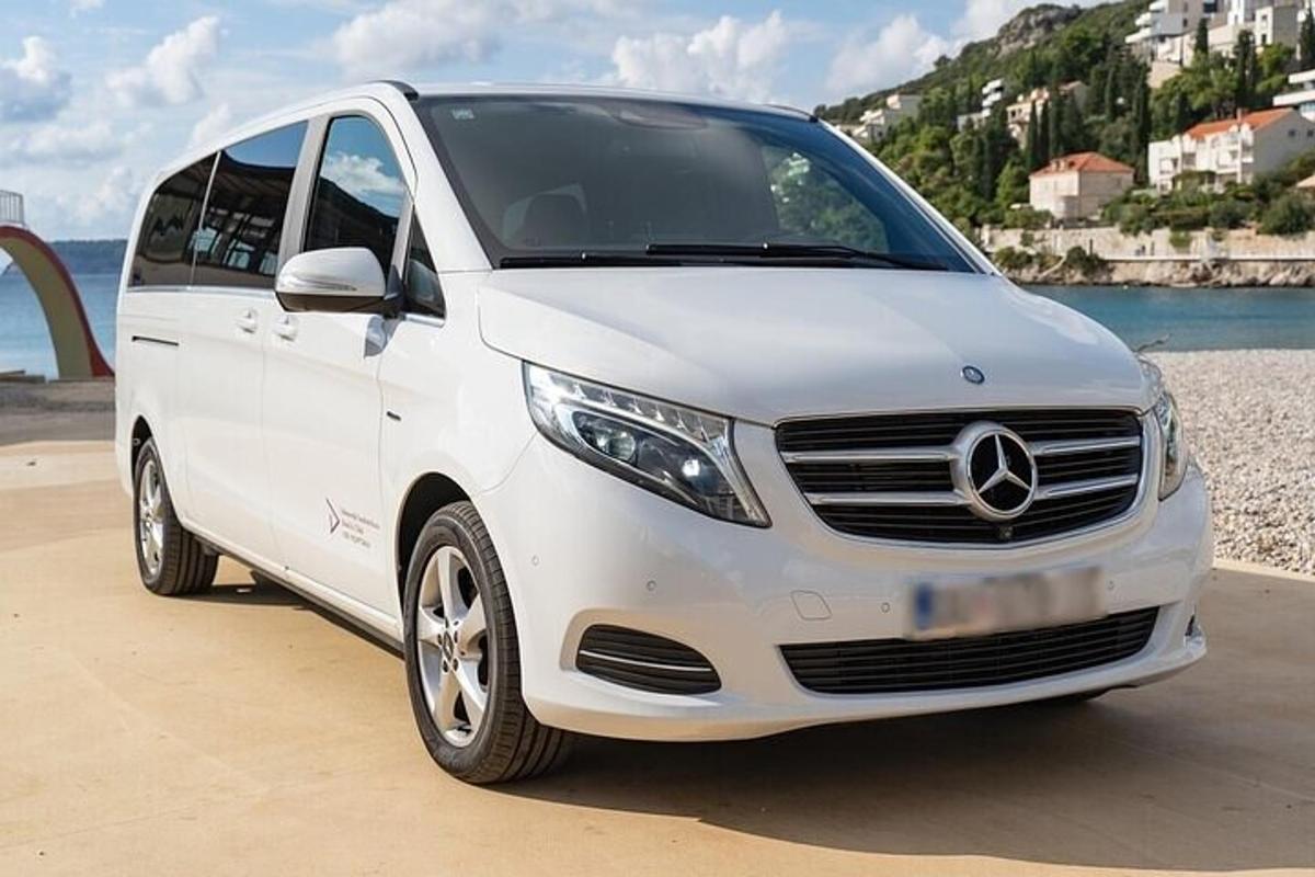 Bílá dodávka Mercedes Benz zaparkovaná vedle pláže