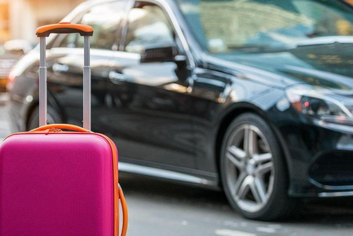a pink suitcase sitting next to a black car
