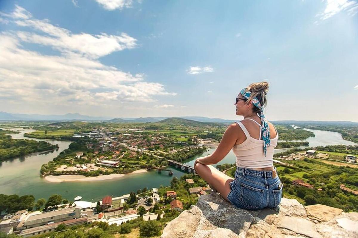 žena sedící na vrcholu skály s výhledem na řeku
