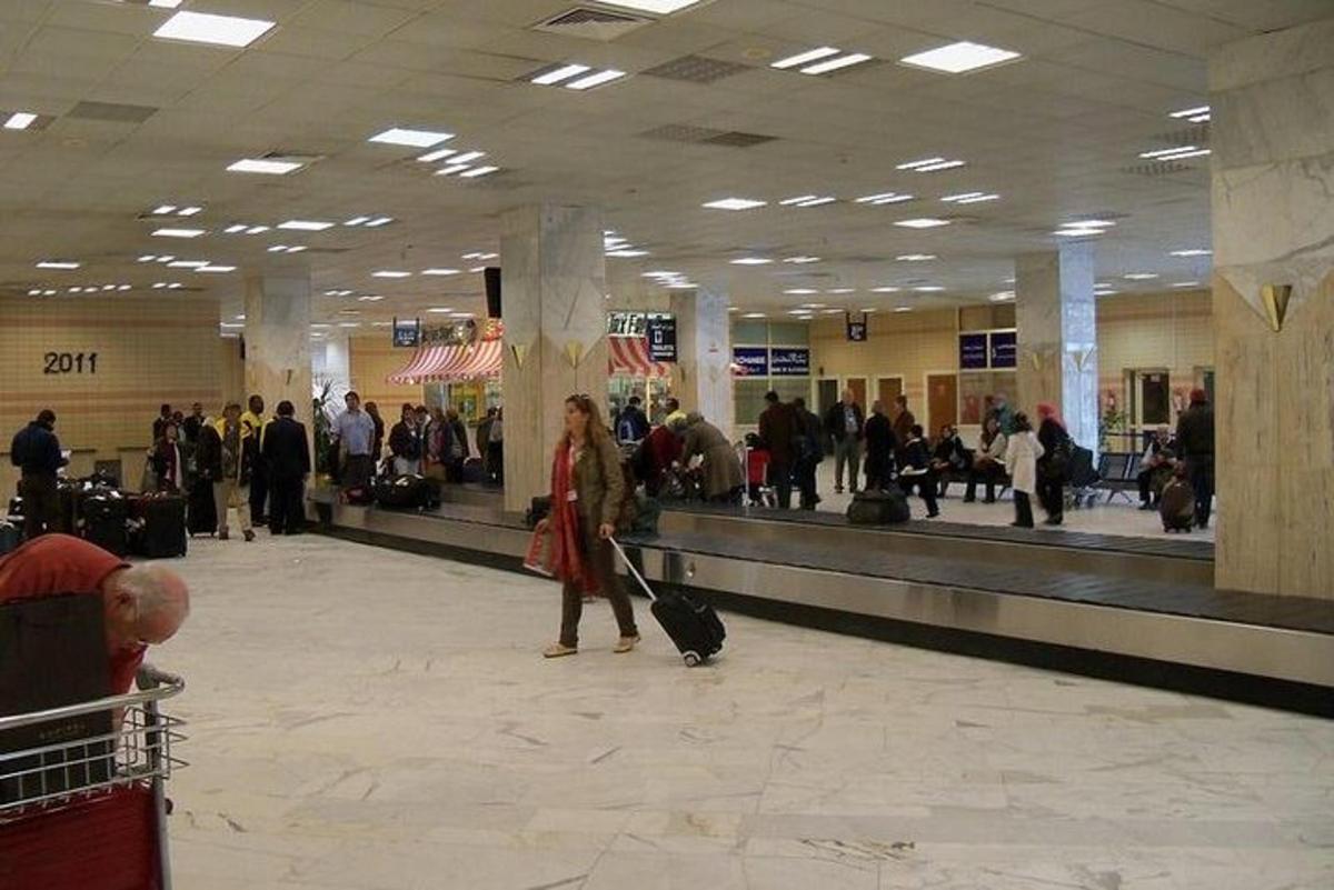 egy nő sétál át a repülőtéren a csomagjaival