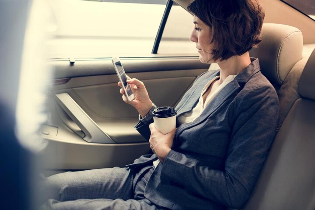en kvinne som sitter i baksetet i en bil og ser på mobiltelefonen sin