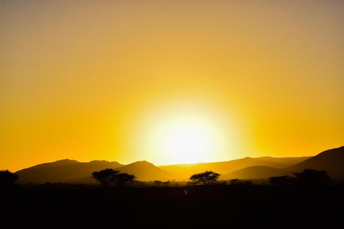 a sunset over a field with mountains in the background