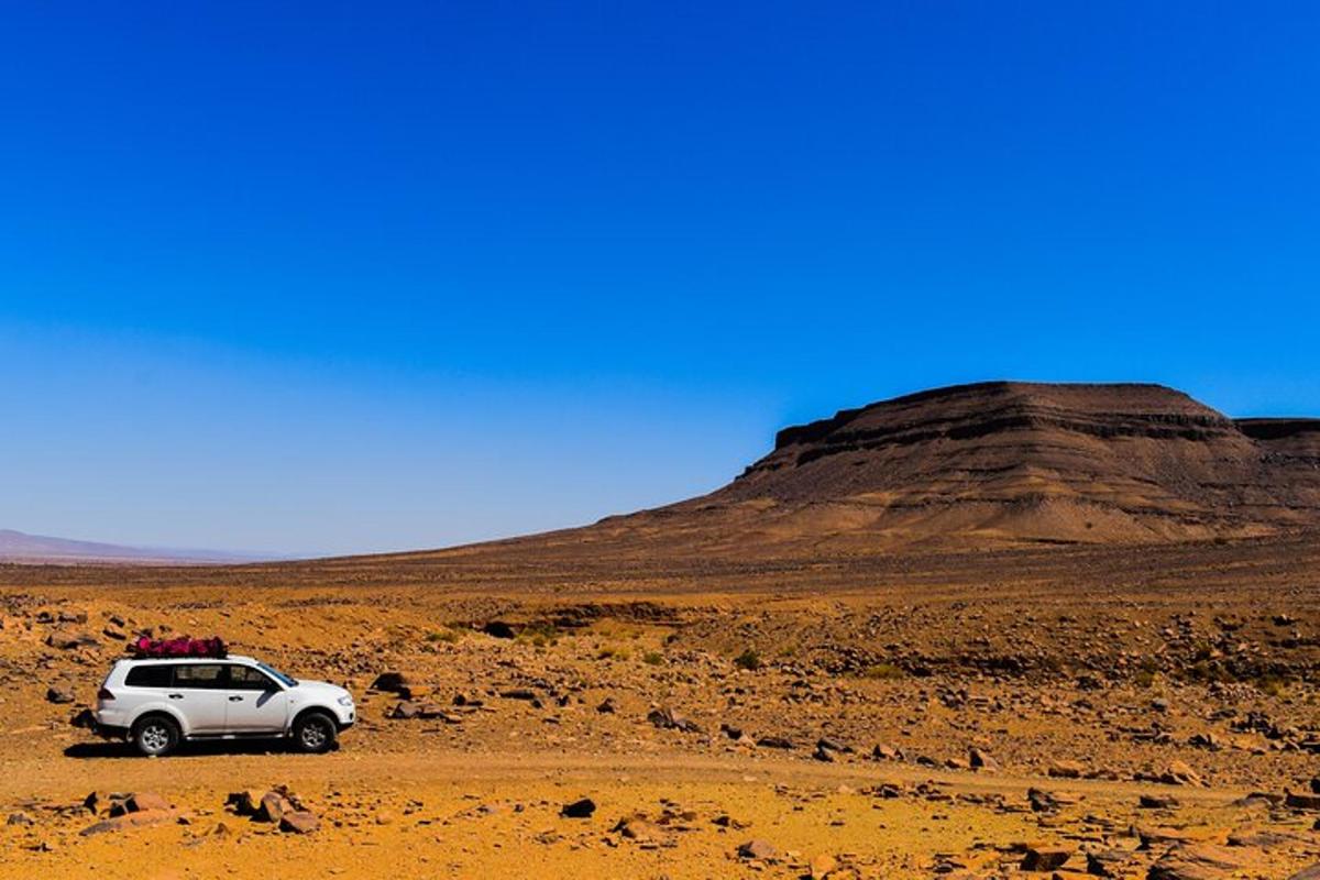a white car parked in the desert with a mountain in the background