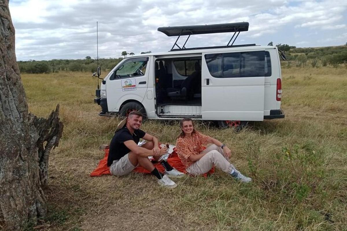 Dos personas sentadas en el césped delante de una furgoneta.