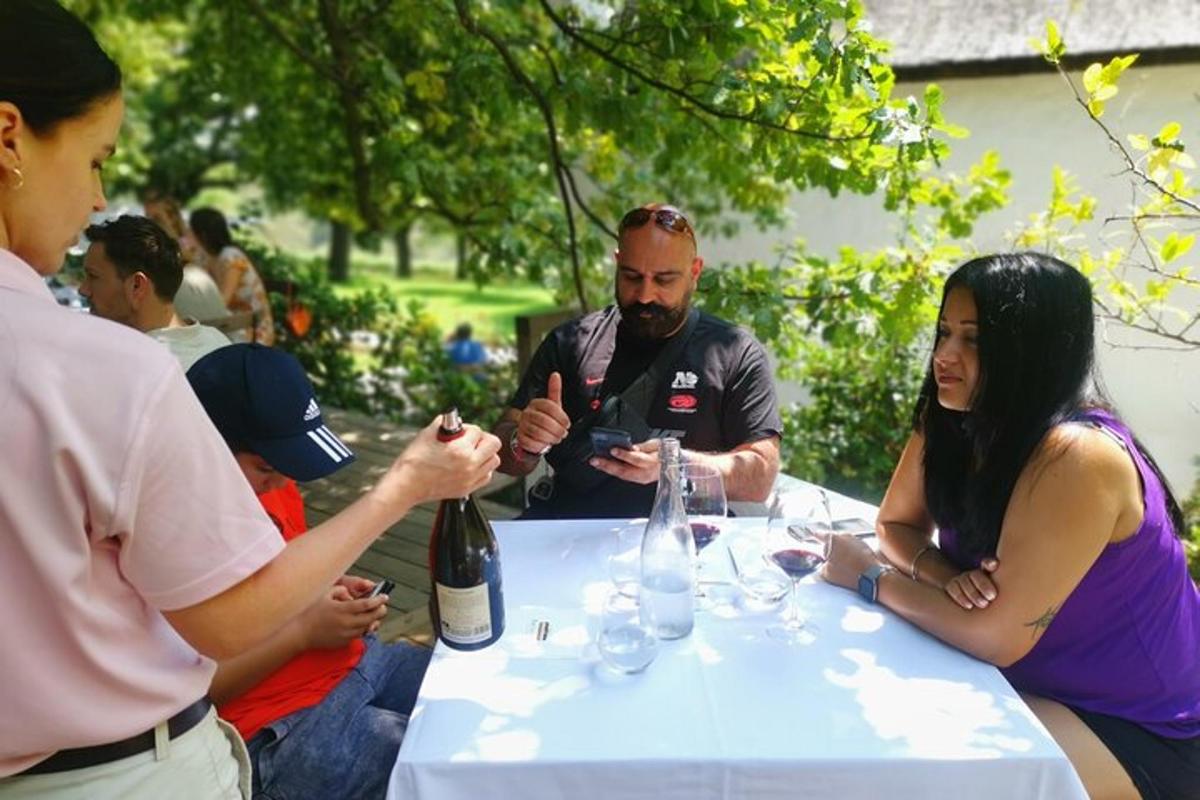 skupina ljudi, ki sedijo okoli mize s steklenico vina
