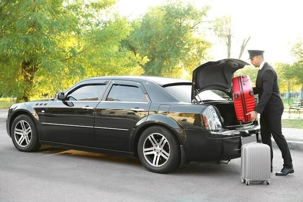 un homme debout à côté d'une voiture noire avec une valise