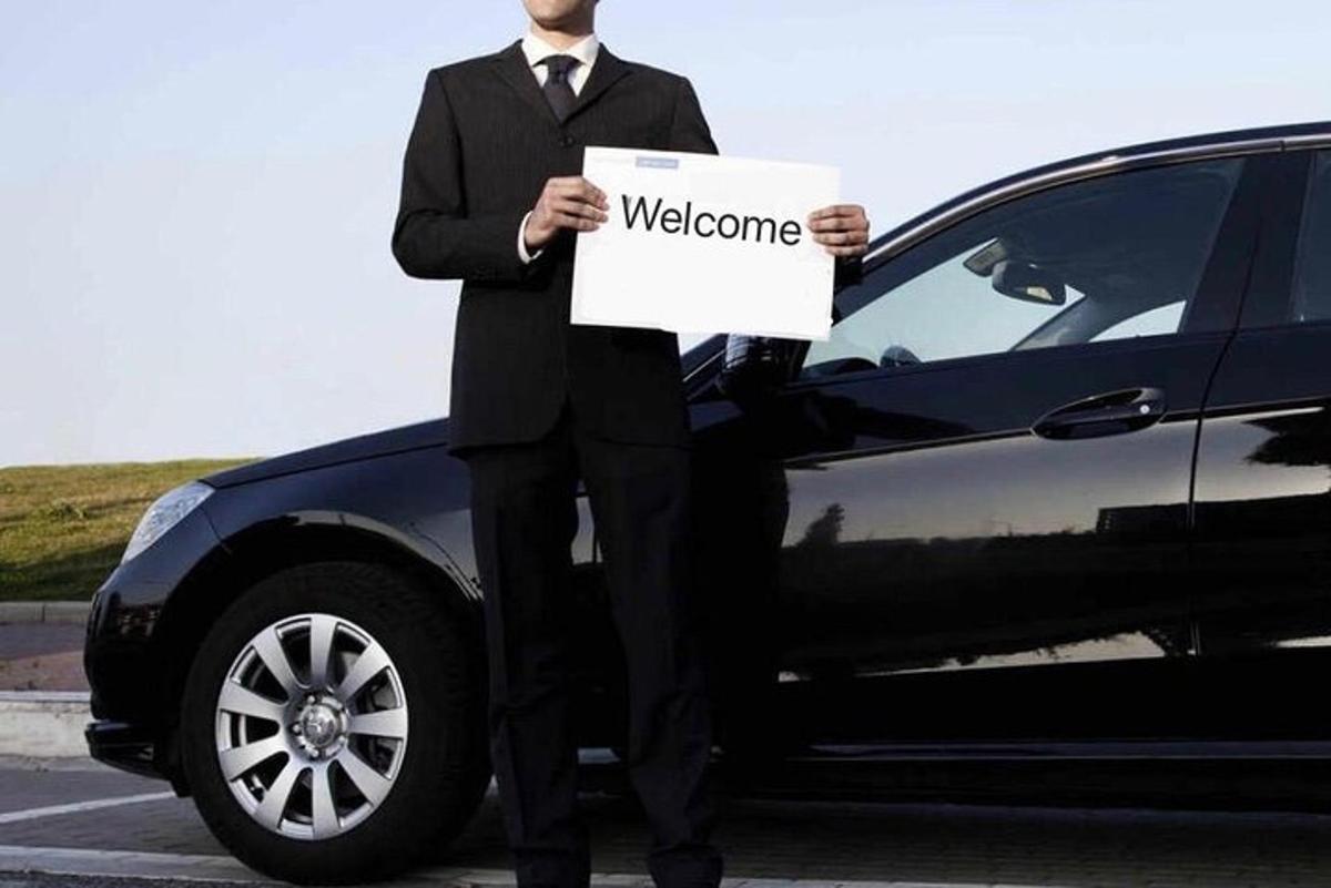 a man in a suit holding a welcome sign in front of a car