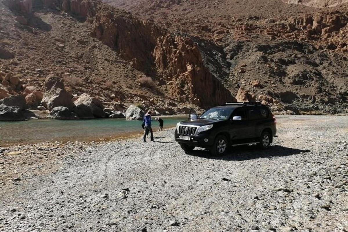 a man standing next to a suv parked on a rocky beach