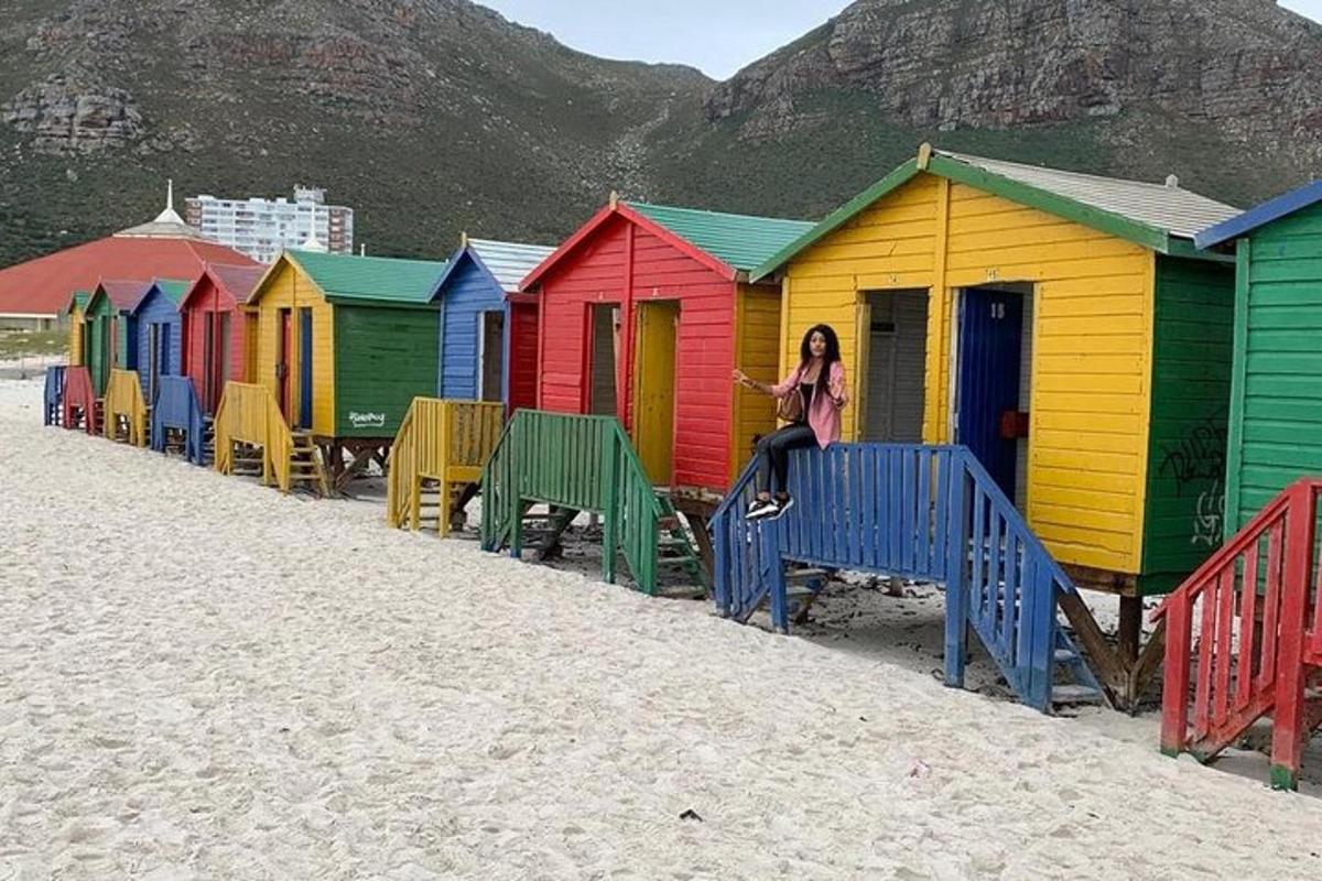 una donna seduta su una panchina di fronte a colorate cabine sulla spiaggia