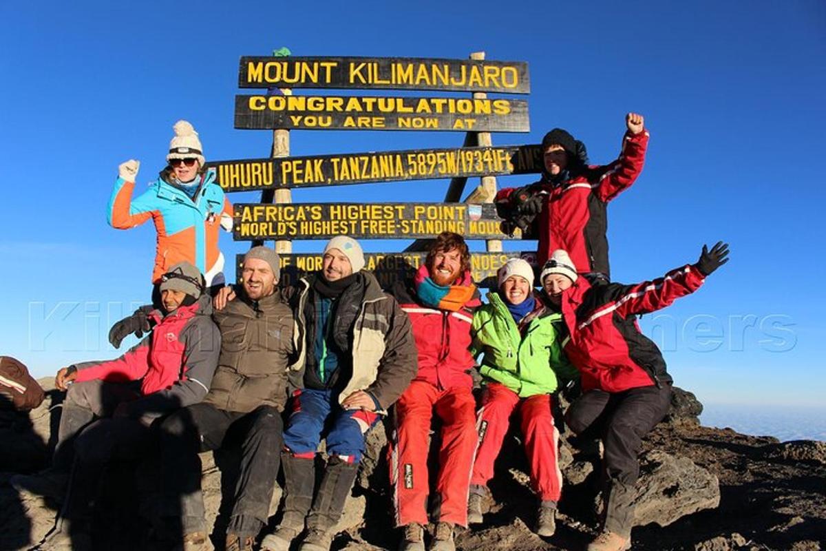 sekumpulan orang bergambar di hadapan papan tanda di atas gunung